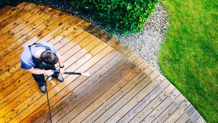 A man pressure washes a wooden deck.