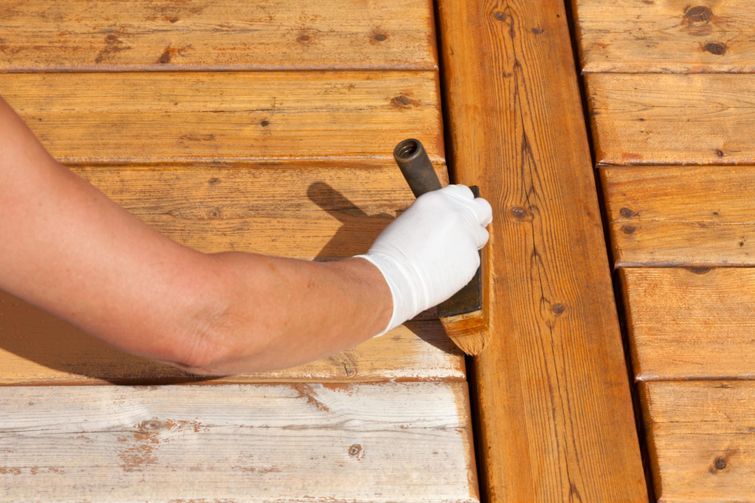 A person with a knife staining a deck wearing white gloves.