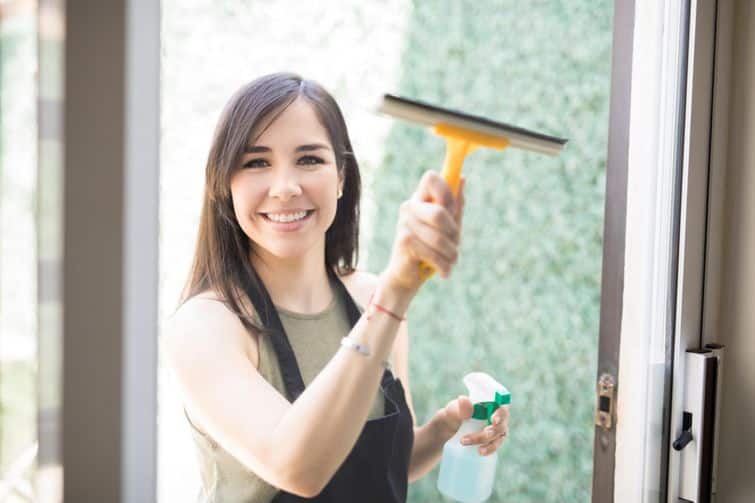 A woman is holding a bottle of cleaner while cleaning windows.