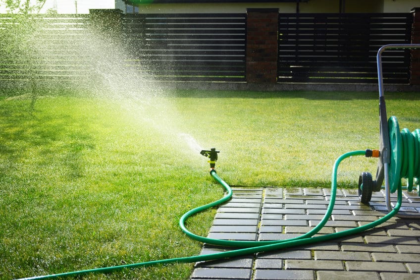 A sprinkler is preventing weeds on a lawn by spraying water.
