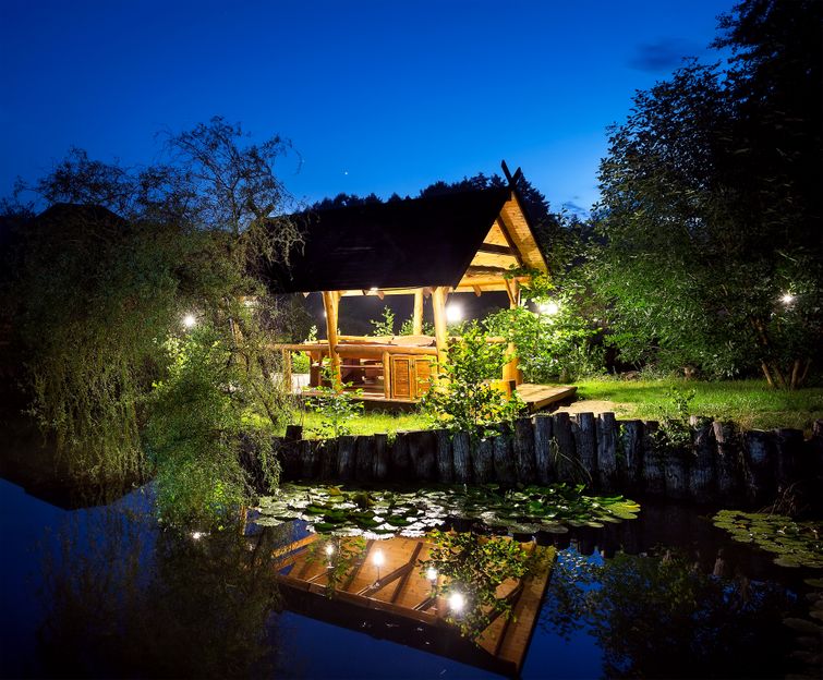 A wooden cabin is illuminated at night by voltage landscape lighting.