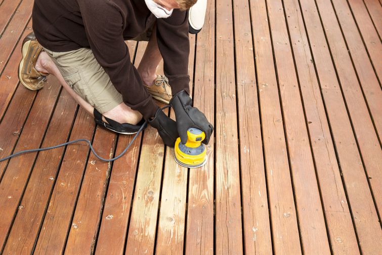 A man using a power sander to refinish a wooden deck.