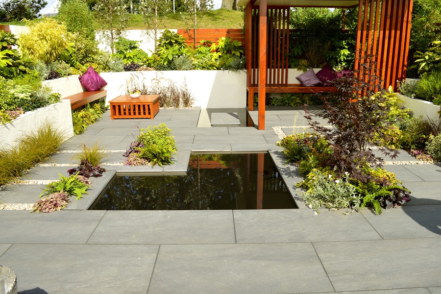 A low-maintenance garden with a pond and wooden benches.