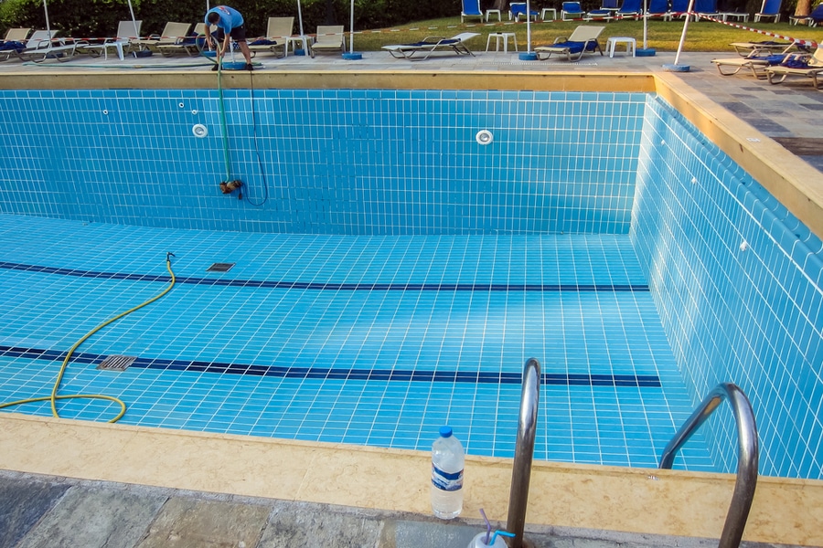 A pool with blue tiles and a ladder that needs to be drained.