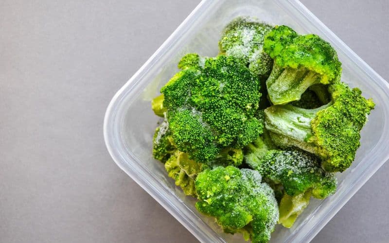 a plastic container filled with green broccoli florets.