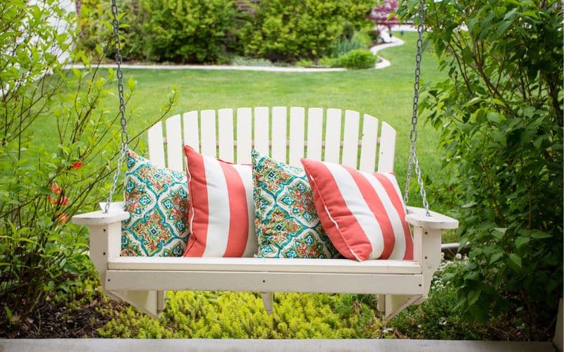 a white swing with pillows on it in a garden.