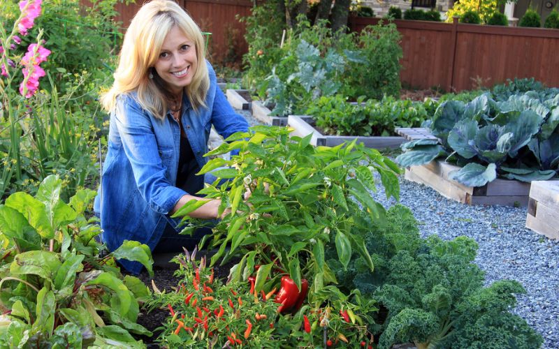 a woman kneeling down in a garden filled with lots of plants and vegetables