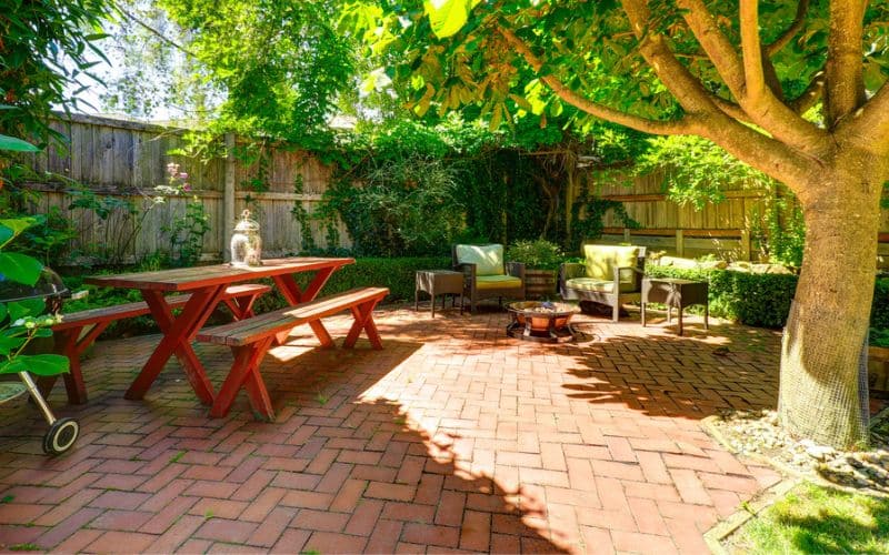 a brick patio with wooden table and trees around