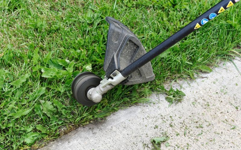 A person using a weed whacker to to trim on wet grass. 