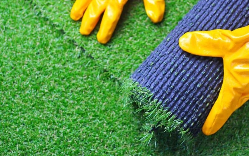 a person wearing yellow gloves is laying artificial turf on the ground.