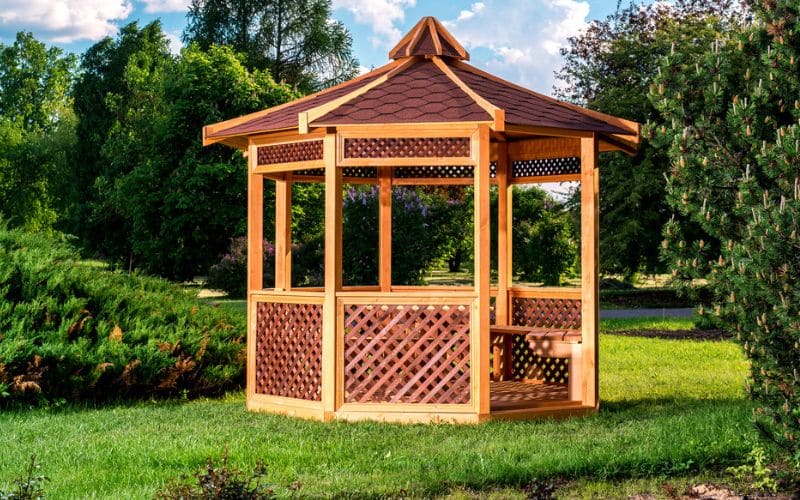 A wooden gazebo arbor in the middle of a park.