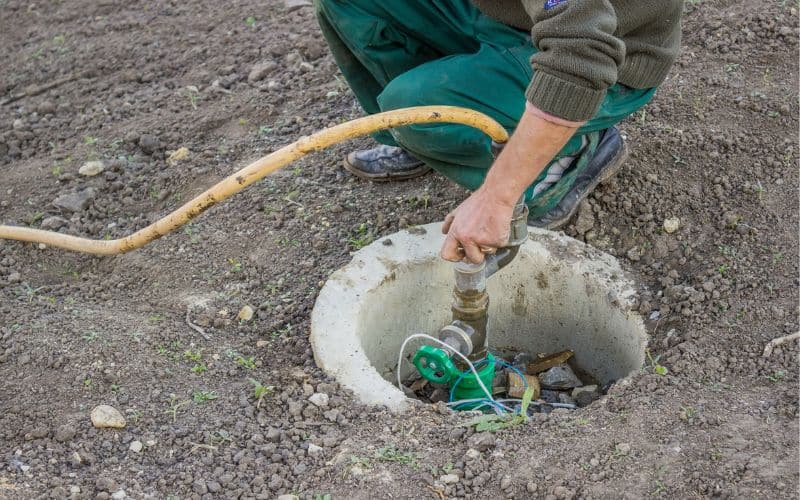 A man putting a garden hose into a hole in the ground.