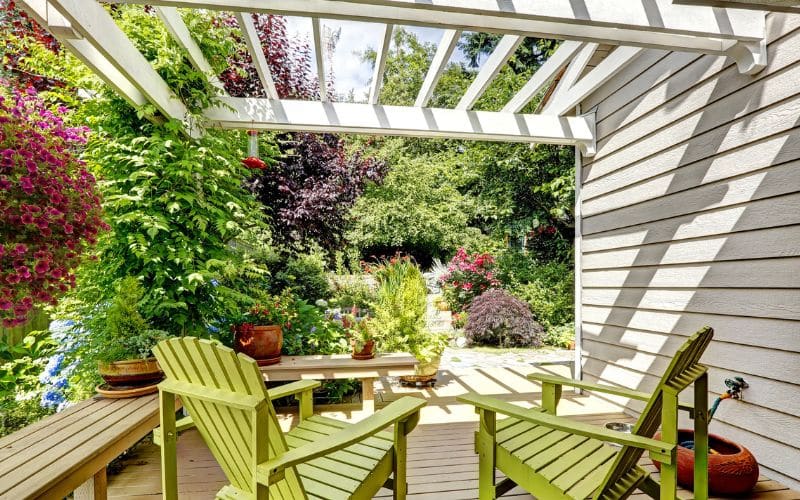 A deck with green chairs and attached pergola.