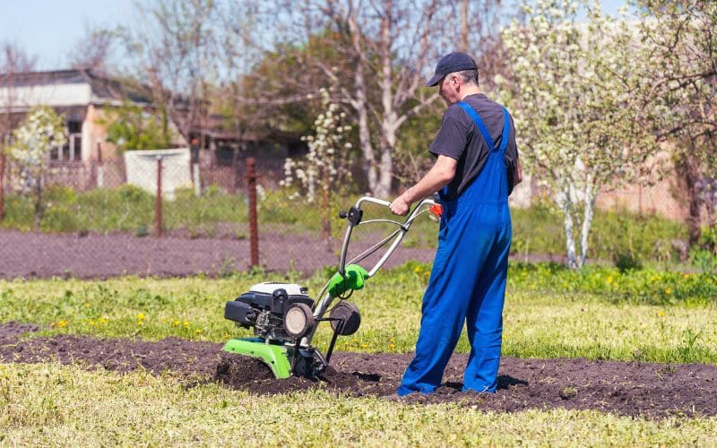 A man in overalls is using a rototillers.