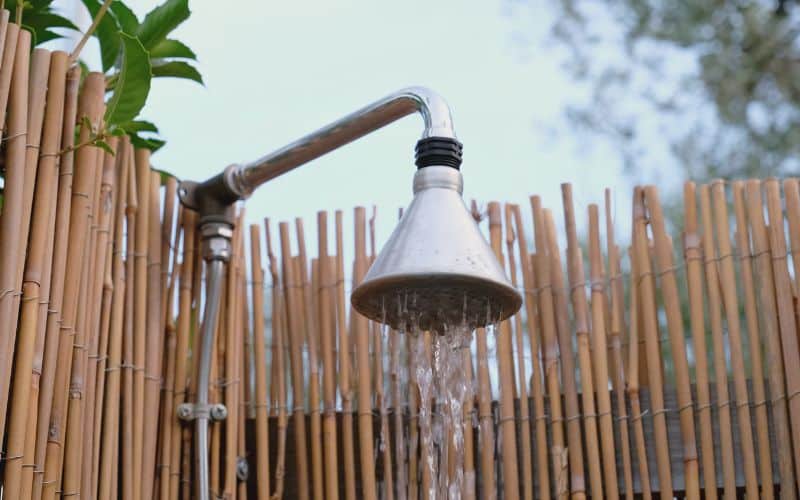 A shower head is coming out of a bamboo fence.