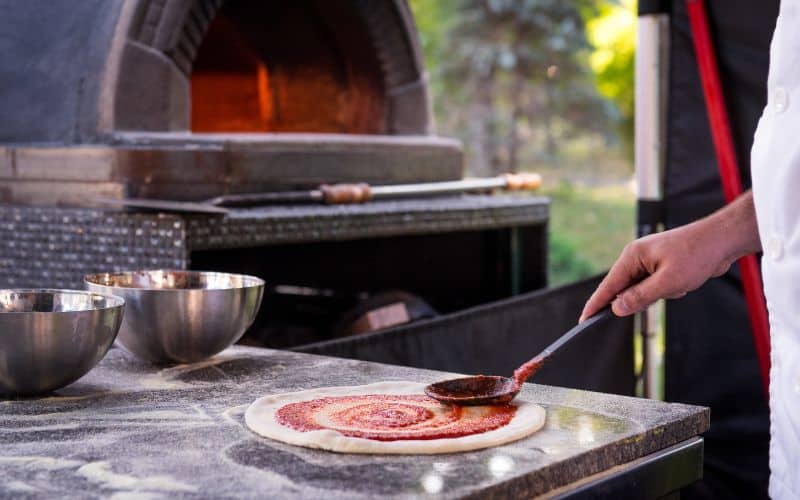 A chef preparing a homemade pizza in an outdoor oven.