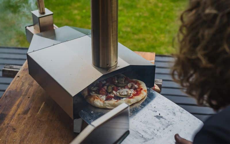 A woman is preparing a pizza in an outdoor pizza oven.