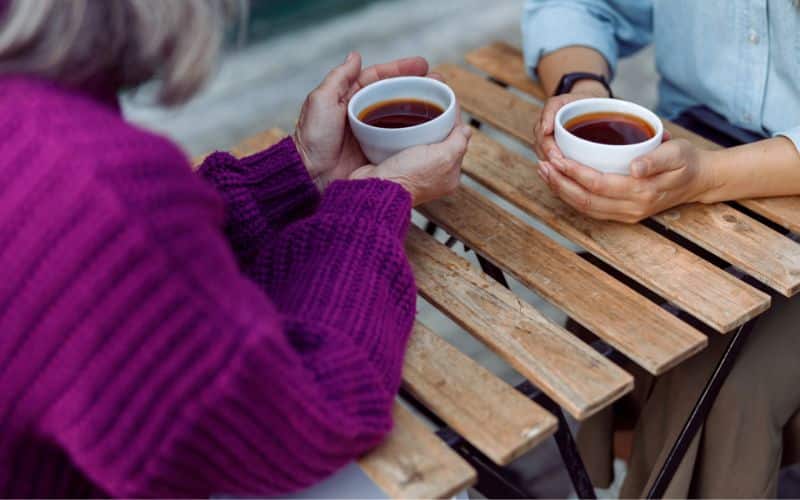 Two older women drinking coffee at an outdoor table.