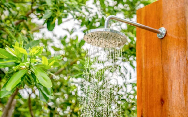 A shower head on a wooden wall with trees in the background.