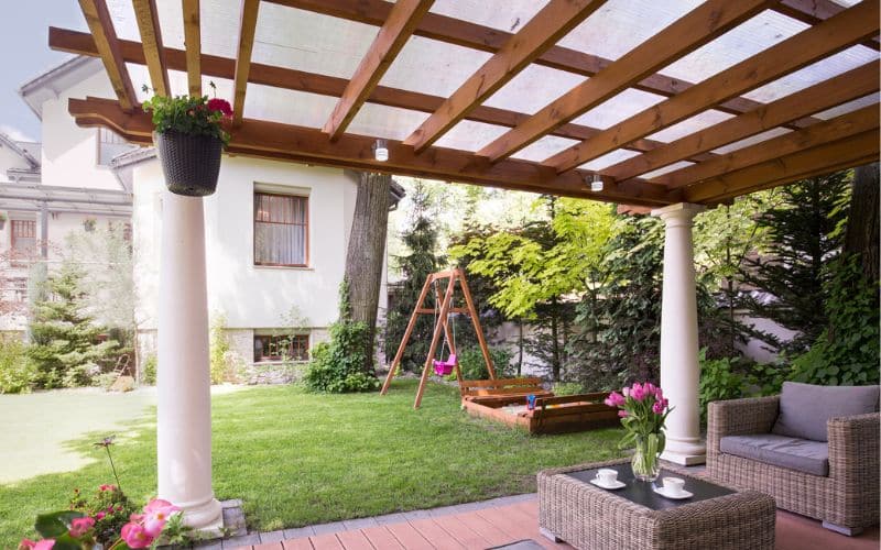 A backyard with a wooden pergola and wicker furniture.