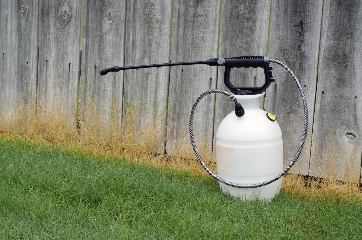 A white sprayer in the grass next to a wooden fence.