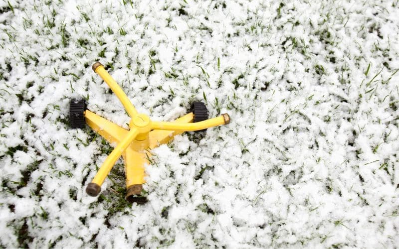 A yellow lawn sprinkler is covered in snow.