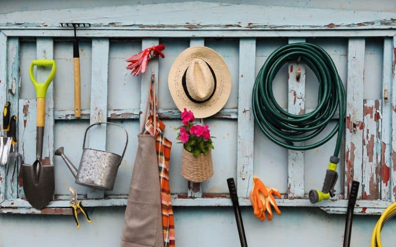 Garden tools and hats hanging on a wooden wall.
