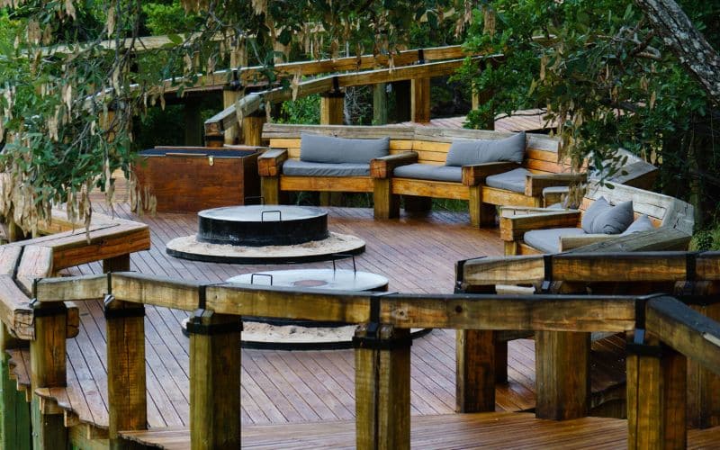 A wooden deck with a fire pit in the middle of the woods.