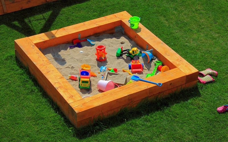 A wooden sandbox with toys in it.