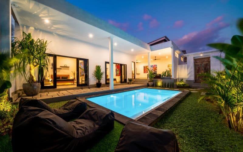 A house with a swimming pool and lounge chairs at dusk.