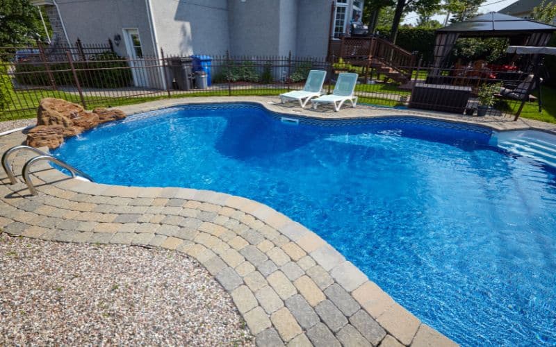 A gunite swimming pool in a backyard with a patio.