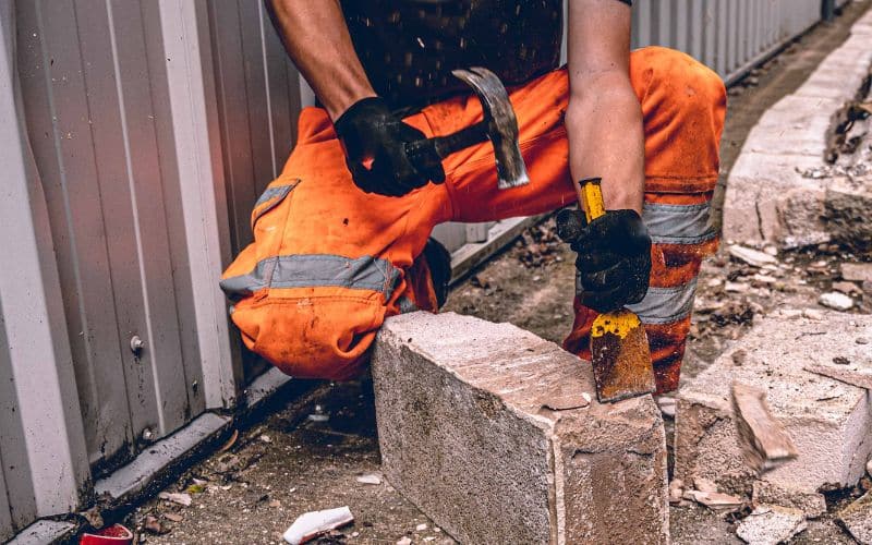 A construction worker is hammering a brick using a chisel
