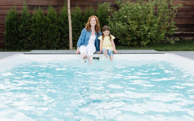 A woman and her daughter sitting in a swimming pool.
