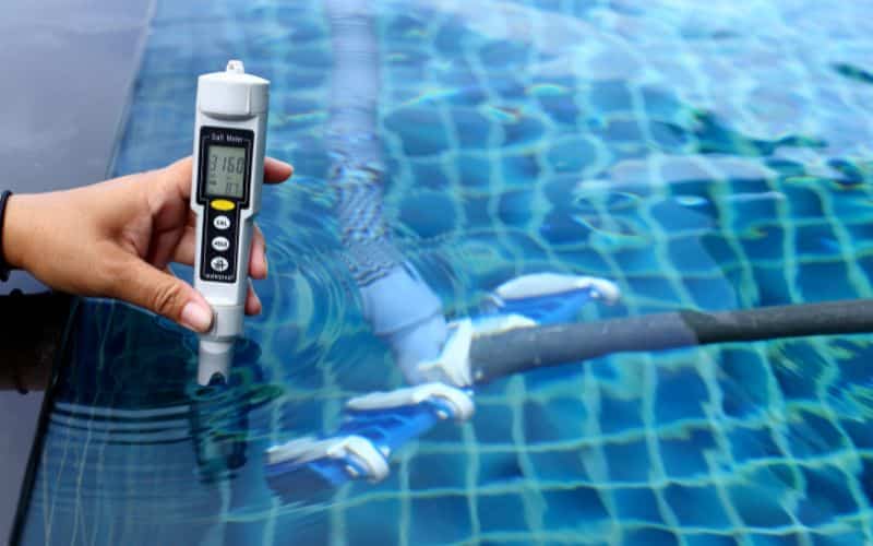 A person holding a salt meter level next to a pool.