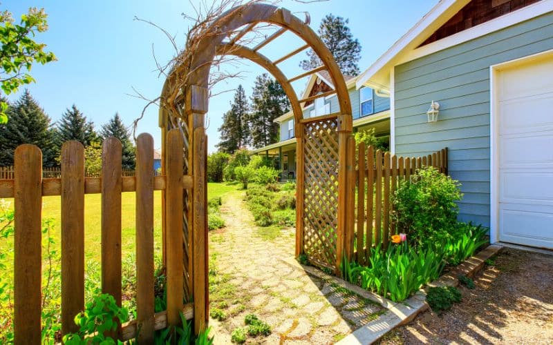 A garden arbor with a wooden gate in front of a house.