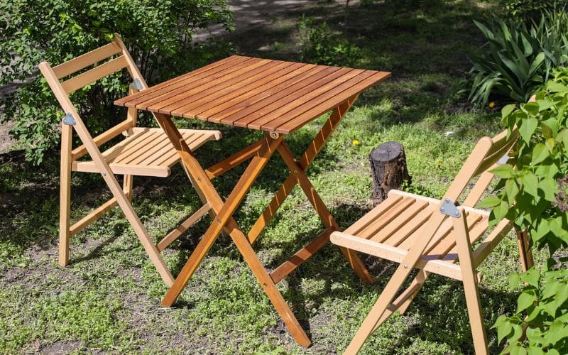 Two folding wooden chairs and a table in the grass.