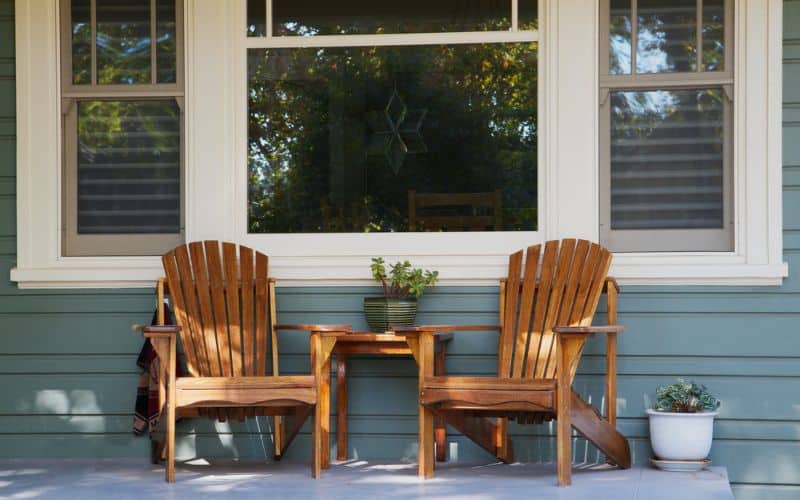 Two wooden adirondack chairs on a front porch.