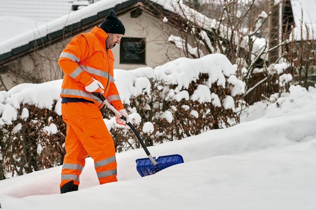 Communal service worker in uniform with a shovel clears snow in winter