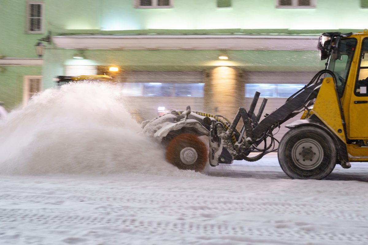 Snow Plow clearing road at night, municipal services cleaning city streets after snowfall in winter